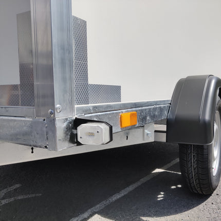 Detail afbeelding van een witte LED breedtelamp van Aspöck (Knott) gemonteerd op het chassis van een gesloten witte aanhangwagen. De aanhangwagen is voorzien van witte reflecterende band op de hoeken. Er zijn zwarte kunststof spatborden gemonteerd. De aanhangwagen is van de fabrikant VDM Trailers te Pelt.